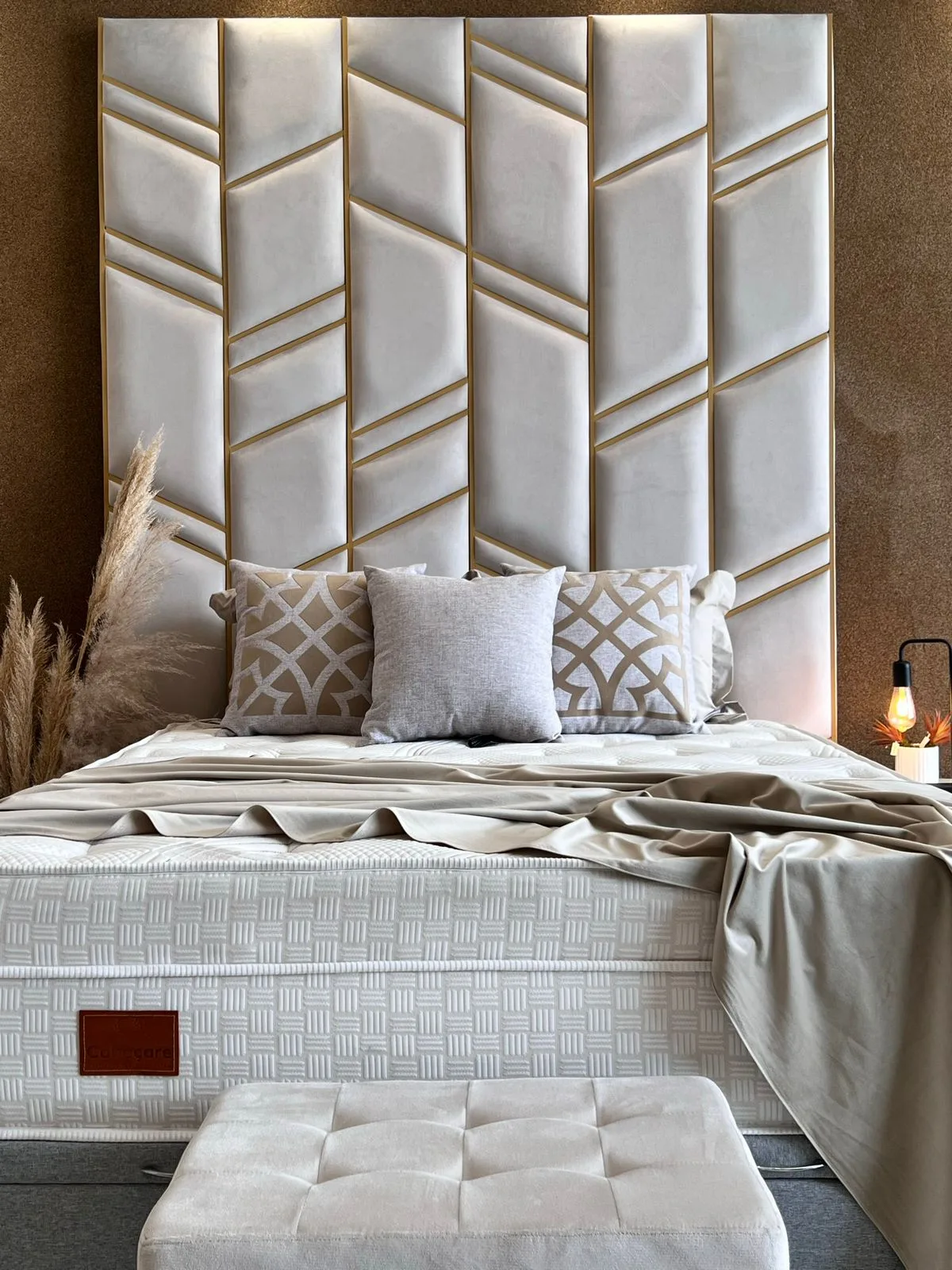 Painel estofado geométrico branco com filetes dourados atrás de cama arrumada