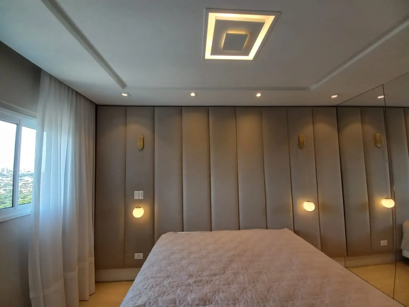 Painel estofado de parede inteira com arandelas douradas e pendentes