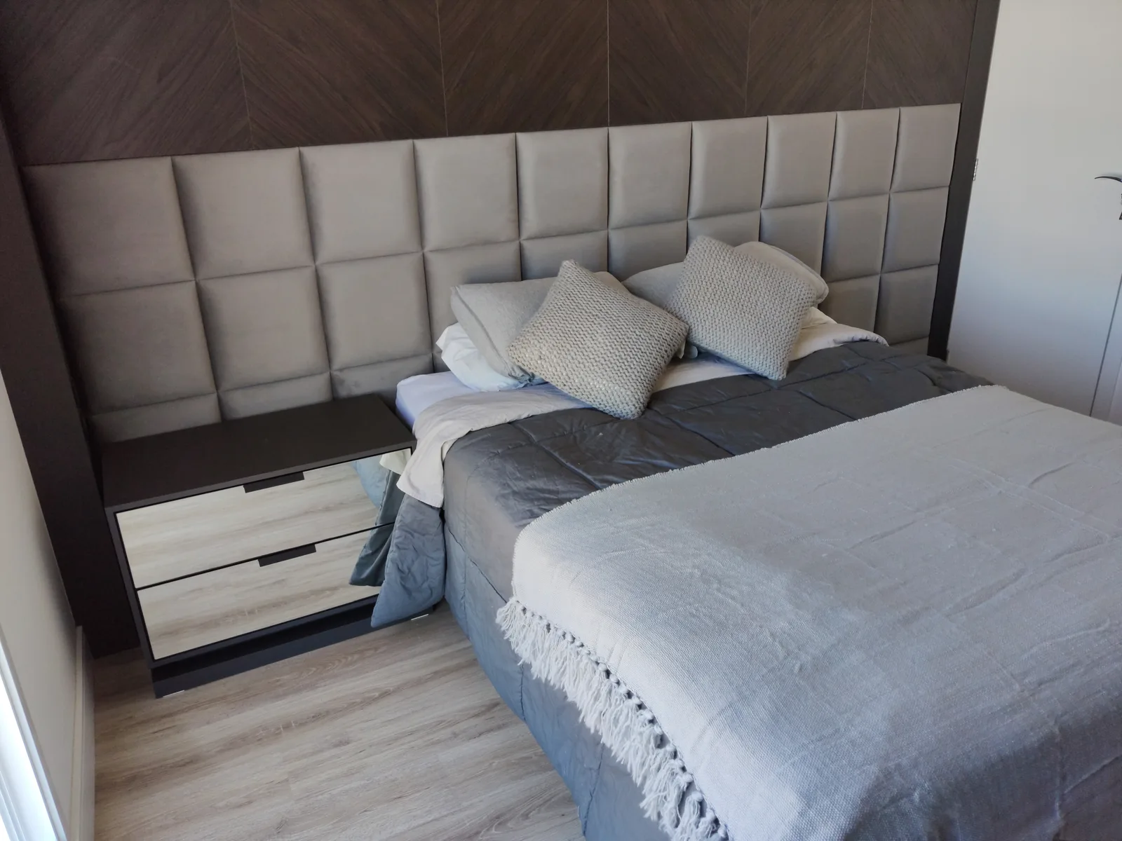Painel estofado de quadros cinza de parede a parede atrás de cama king